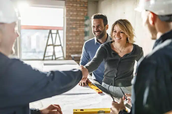couple shaking hands with building contractors