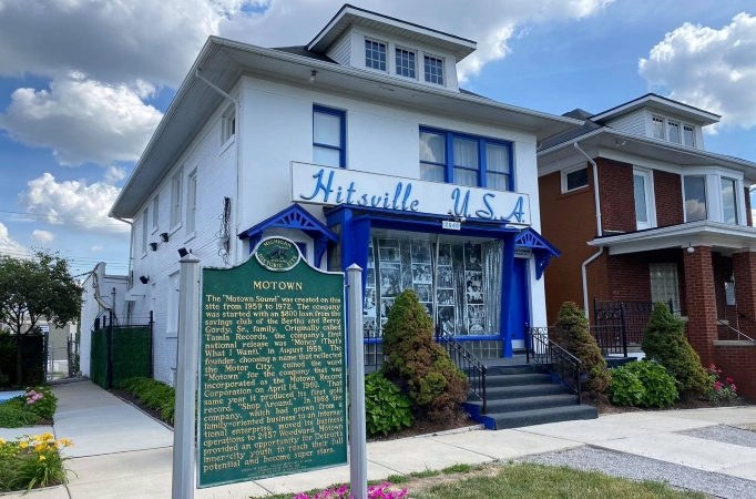 The Motown Museum in Detroit, Michigan. It’s a white building with a blue entrance. A sign that reads “Hitsville U.S.A.” is above the door, and there’s a historic MOTOWN plaque in front of the building. 