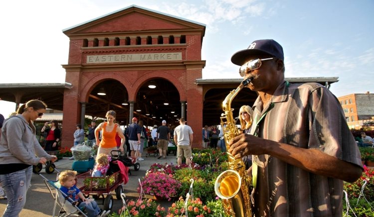 A man is playing saxophone outside Detroit’s Eastern Market as locals enjoy a sunny day exploring all the market has to offer. 