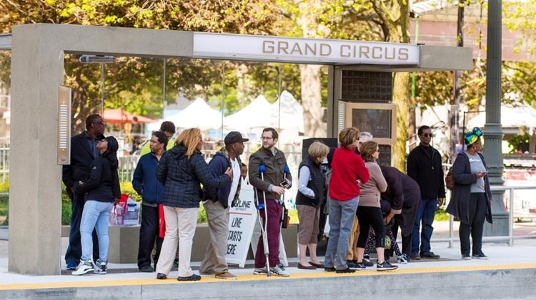 More than a dozen people are waiting at the Grand Circus bus stop in Detroit, Michigan. 