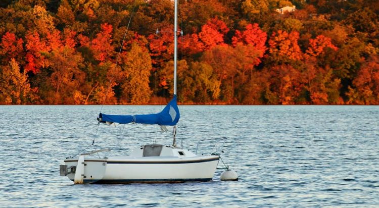 A sailboat on Lake Harriet in Minneapolis during autumn. The trees on the shoreline are a striking rainbow of oranges, reds, and yellows