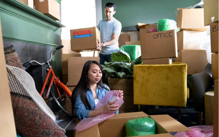 A young couple packing up their homes, surrounded by cardboard boxes