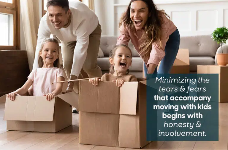 Young parents are pushing their two young daughters across the floor in empty moving boxes. The overlaid text reads, “Minimizing the tears & fears that accompany moving with kids begins with honesty & involvement.”