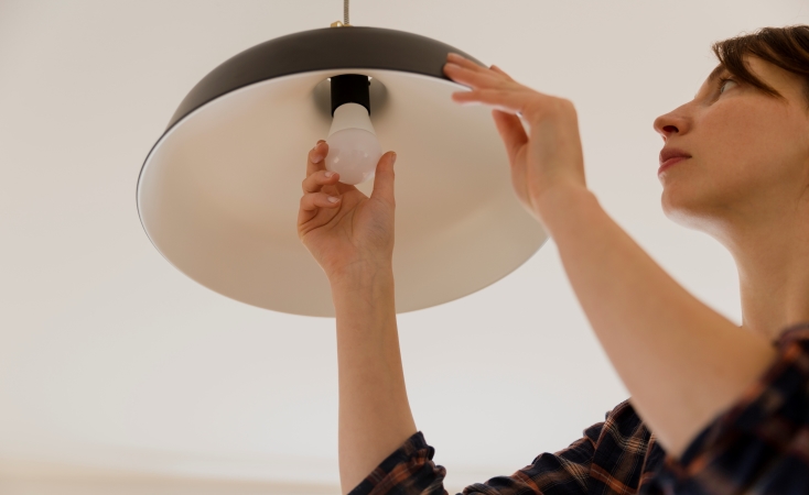 A woman is replacing the lightbulb in a hanging lamp.
