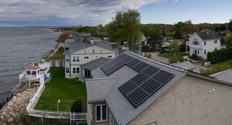 A large waterfront home with solar panels on the roof, making the home more energy-efficient.