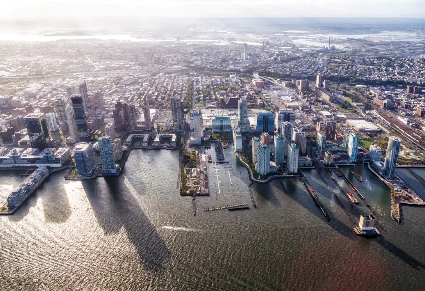 Aerial view of the Jersey City skyline. Skyscrapers dot the water’s edge, and the rest of the densely populated city sprawls inland.