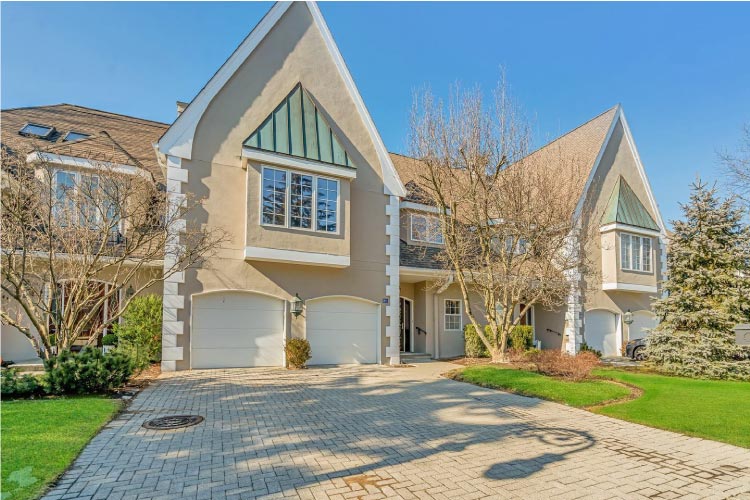 A large, single-family home in Ho-Ho-Kus, New Jersey, features a two-car garage, steep gables, and a stucco exterior.