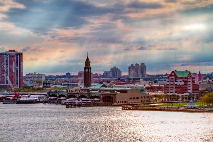 The Hoboken, New Jersey, waterfront just before sunset. The cloudy sky is pastel colored and rays of light are streaming down upon the city. 