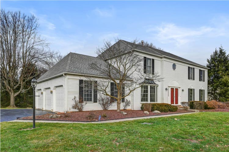 A large Colonial-style house in Princeton Junction, New Jersey, featuring a white siding exterior, black shutters, and a red front door.