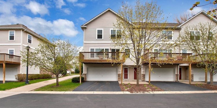 View of a few townhomes in a neighborhood in Northeast Minneapolis. The homes feature three stories with a two-car garage on the ground floor and a large wooden deck above the garage. 