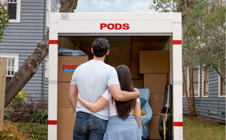 A couple standing in front of their loaded PODS container with their arms around each other.
