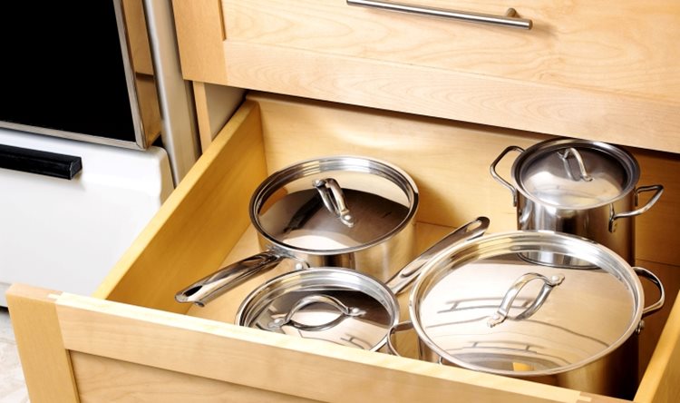 A kitchen drawer that is left open, exposing its contents — a set of shiny metal pots with matching lids.