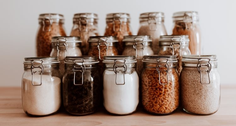 Fourteen glass storage jars filled with dry goods and organized into three neat rows with the tallest jars in the back and the shortest ones in the front.