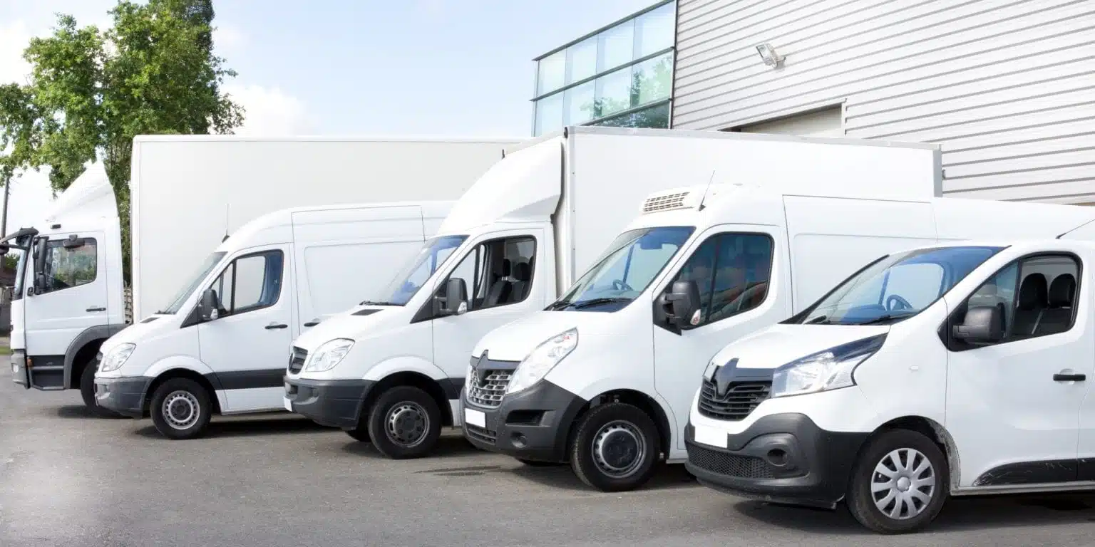 Five different types of white moving trucks and vans are parked in a row, making it easy to see the differences in rental moving truck sizes.