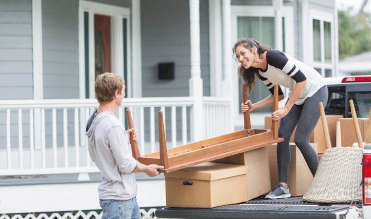 A happy couple is loading furniture and boxes into the back of a pickup truck.