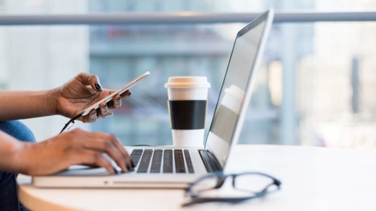 Close-up view of a woman’s hands as she uses her cell phone and laptop to access a moving calculator and budget out her upcoming move.