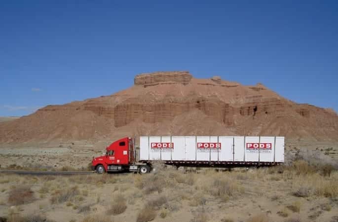 A PODS truck is transporting three PODS portable moving containers along a freeway in an arid part of the country.