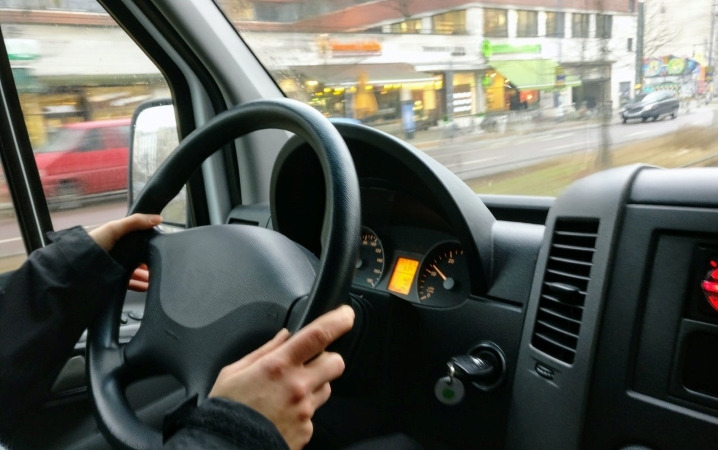 Close-up of a man’s hands holding the steering wheel of a moving truck as he navigates through a city.