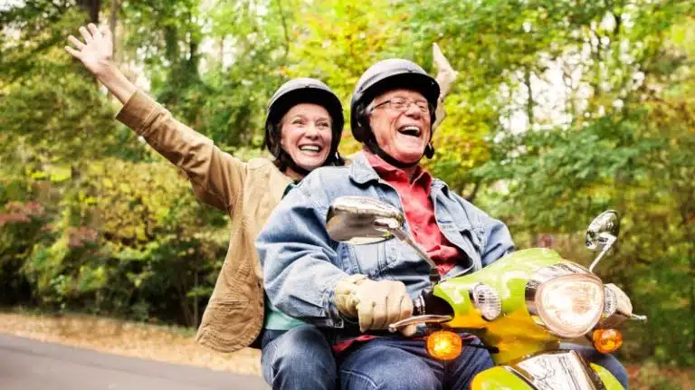 A happily retired couple riding together on a moped down a tree-lined road in one of the best states to retire.