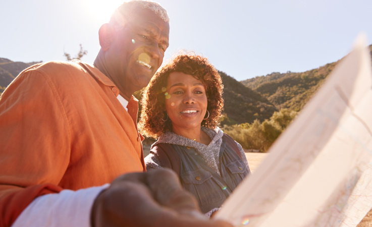 A couple is looking at a map together as the sun shines down from over their shoulders. They’re traveling to different states to figure out where they want to retire.