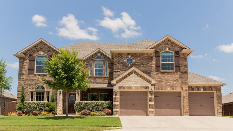 A lovely two-story, brick home in Helotes, Texas. The home is very large and appears to be almost entirely brick. Some stone facades are used as an accent on either side of the entrance and above one of the three garages.