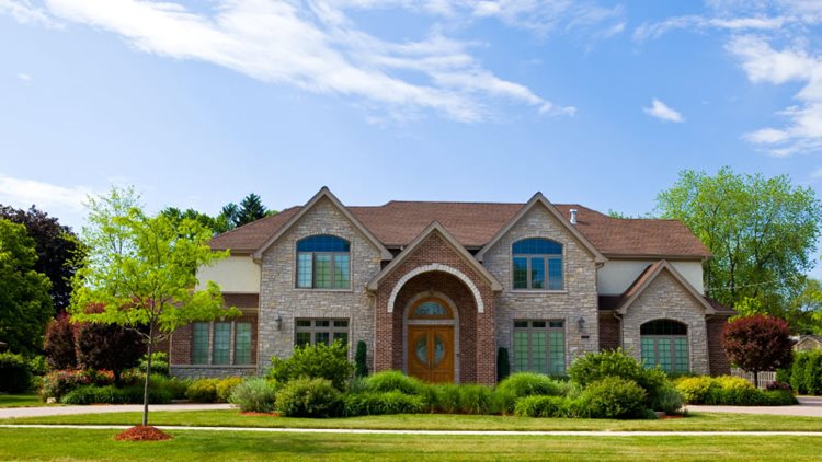 A large, single-family home in San Antonio’s Alamo Ranch community. The house is newly constructed and features both brick and stone-facade elements in the front, as well as multiple gables. The entrance is a covered brick archway leading to large, double doors.