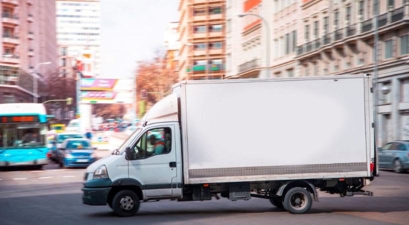A white moving truck is navigating its way through a big city.