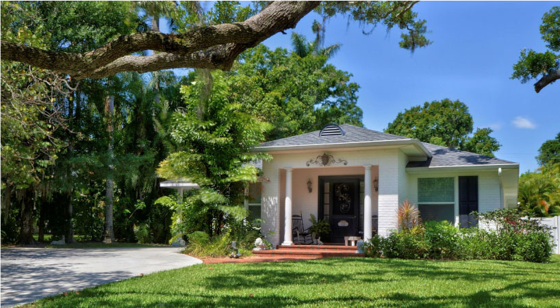 A white, single-story home in Bradenton River District with an ornate light fixture and rocking chair adorning the front porch.