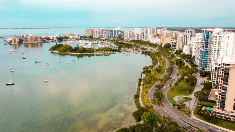 An aerial shot of downtown Sarasota, with numerous high-rise buildings on land and several boats in the surrounding water