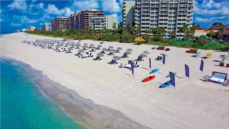 A typical morning Longboat Key beach scene, with umbrellas, chairs, and kayaks set up for the day in front of high-rise condominium buildings.