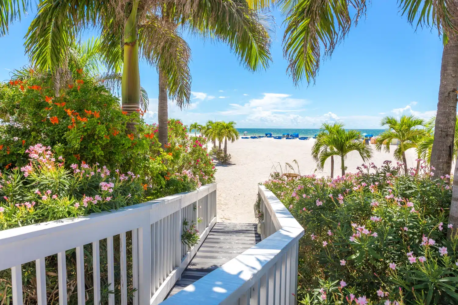 An upscale beach walkway, with tropical flowers and palms on either side, opens up to the white sands and blue waters of St. Pete Beach in Florida.