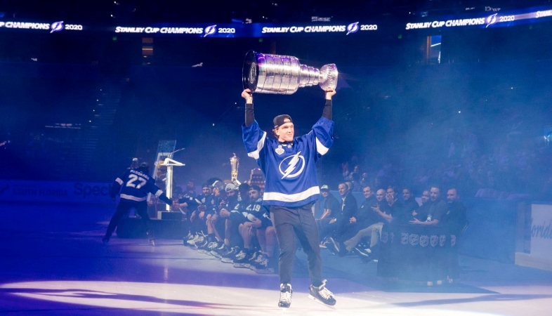 A player from the Tampa Bay Lightning is skating in front of a stadium crowd as he holds the Stanley Cup above his head in celebration.
