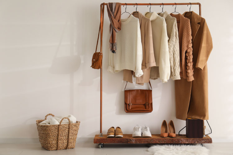 A trendy wood and copper clothing rack with several sweaters and jackets hanging up. There are matching purses and shoes displayed on the rack, as well. 