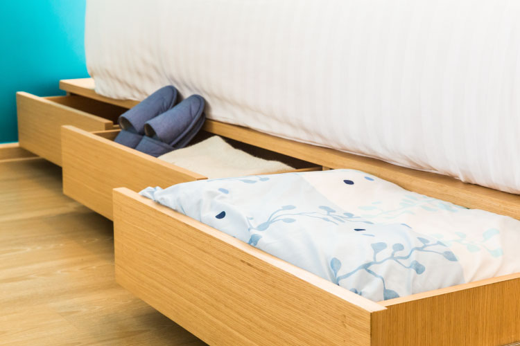 View of the side of a bed, featuring three pull-out drawers. The middle drawer is being used to store house slippers.