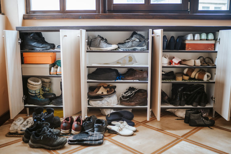 Close-up view of a set of short cabinets used to store shoes. The cabinet doors are all open and the shelves are overflowing with shoes. Several pairs of shoes are also on the floor.