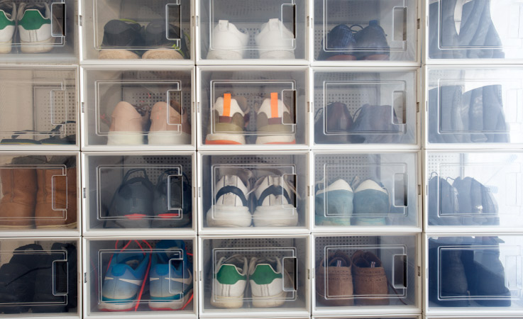 A collection of clear, plastic shoe bins lined up and stacked with different types of shoes neatly organized inside. You can clearly see the shoes, and they appear to be easily accessible, making this one of the best ways to organize a shoe collection. 
