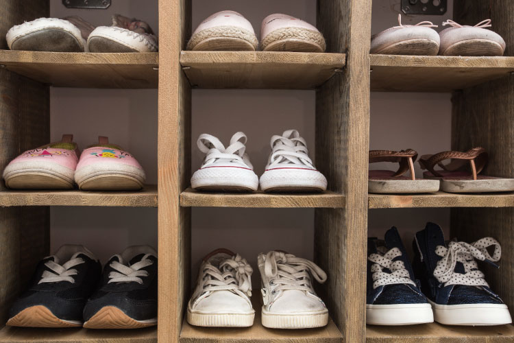 Rough wooden cubbies with nine pairs of sneakers, sandals, and slippers neatly stored inside.