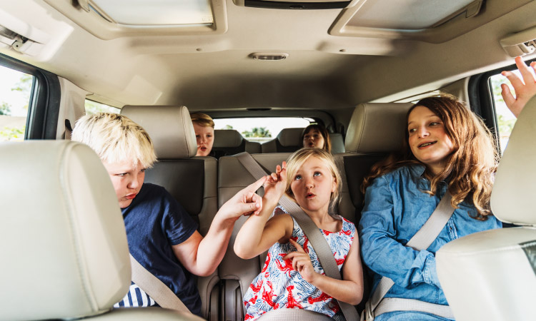Five young kids are buckled up in a minivan ready for a road trip.