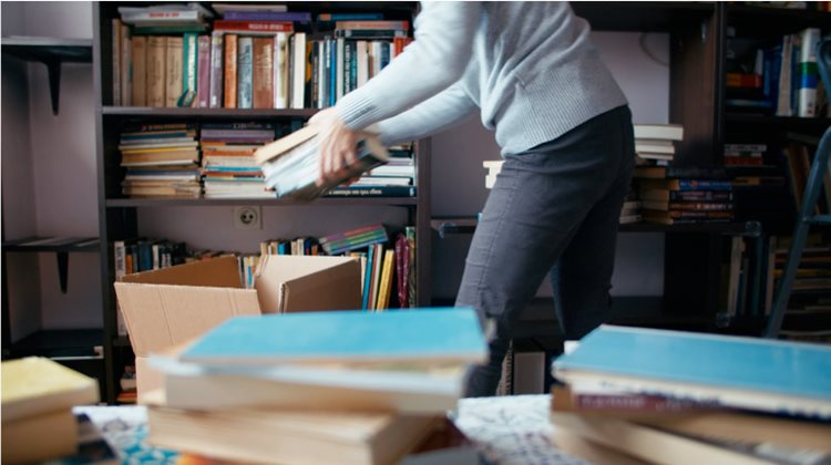 An adult is packing books from their large library into moving boxes.