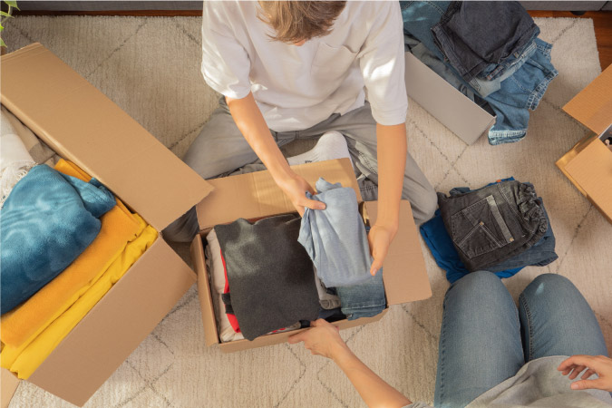 Top-view of a young boy packing his clothes in moving boxes as his mother helps.