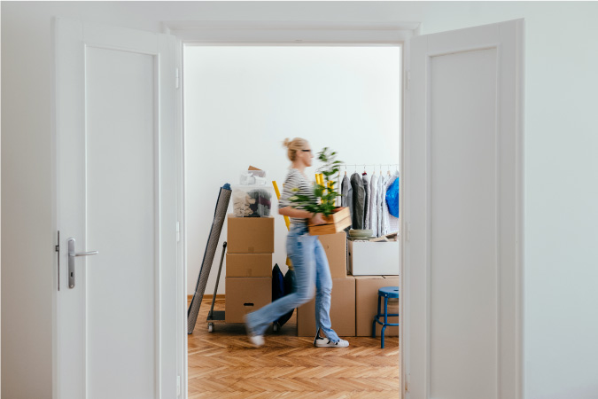 A woman walks quickly past a neatly stacked pile of moving boxes as she packs for her upcoming move with the help of a moving packing list.