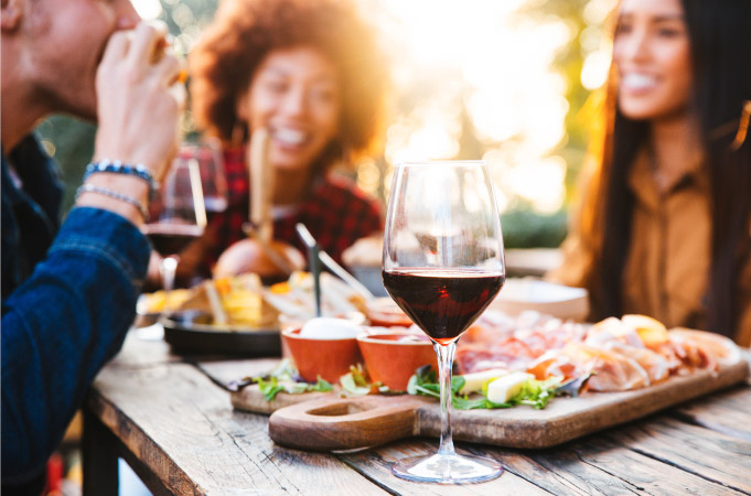 Friends enjoy a meal al fresco in Wilmington, North Carolina. A charcuterie board and glasses of wine are among the many delicious offerings gracing the wooden table. 