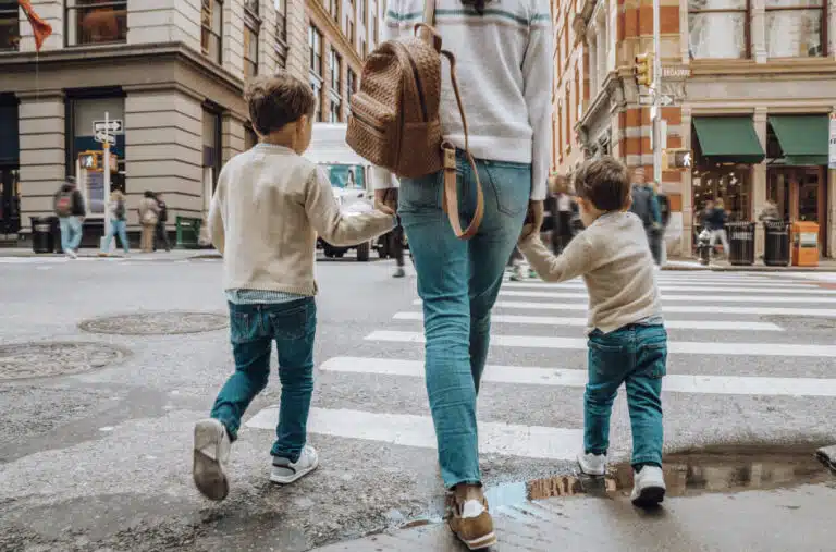 A mother and her two young sons are crossing a street in Manhattan, New York City, on an overcast day.