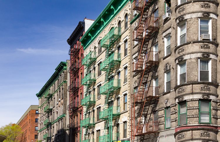 A street-level view, looking up at a row of colorful and historic residential buildings at the intersection of Mott and Kenmare Streets in Manhattan’s NoLita neighborhood.