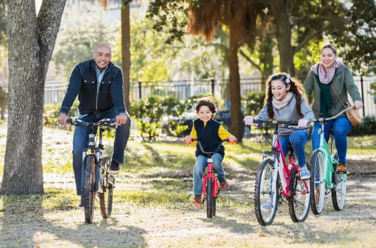 A happy family of four riding bikes through a park in Jacksonville, Florida.