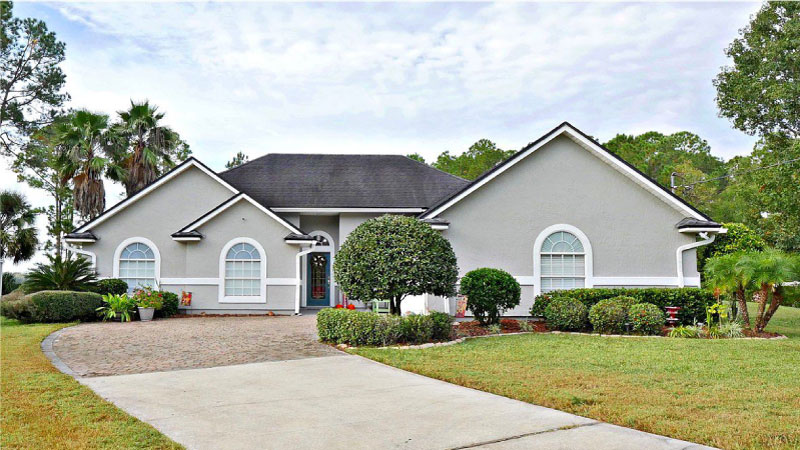 A gray, one-story home in the Eagle Bend Island neighborhood of Jacksonville, Florida. There is a wide, curved driveway leading up to the entrance of the home and a nicely tended yard.