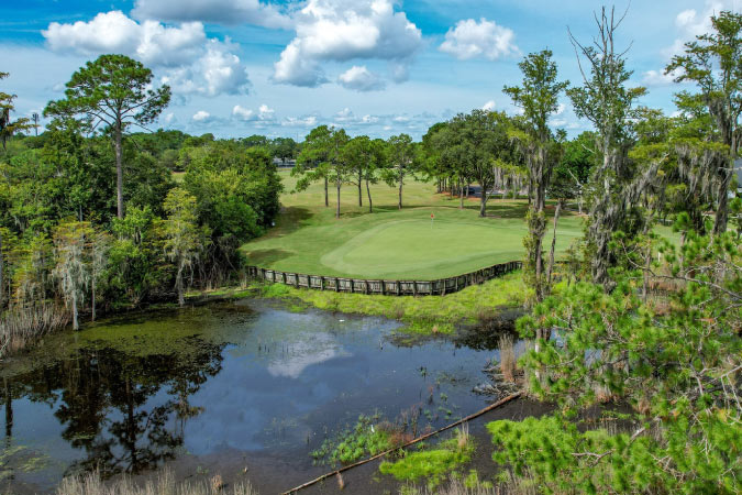 Sunny view of the Deercreek Country Club in Jacksonville, Florida, featuring a pond surrounded by tall trees draped in Spanish moss.