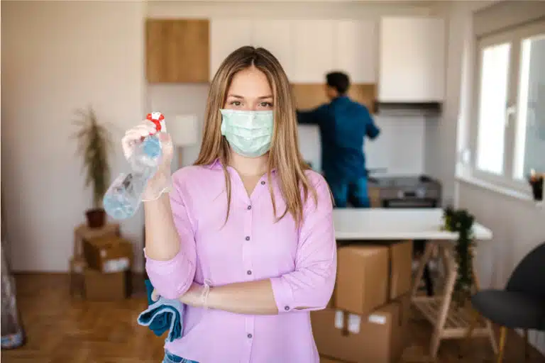 woman holding cleaning supplies while wearing mask with moving boxes
