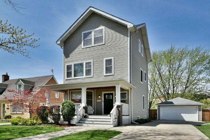 A three-story home with gray siding exterior, detached garage, and a covered front porch, in the Chicago neighborhood of Norwood Park.
