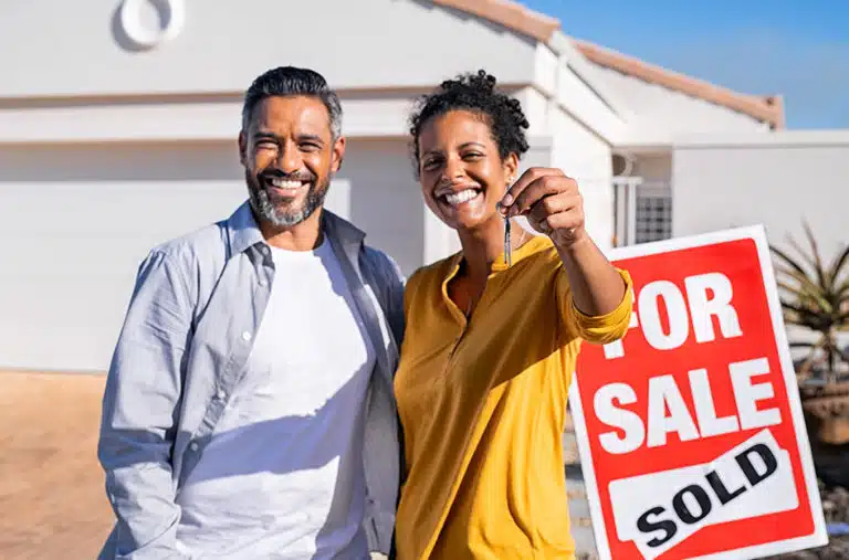 new homeowners holding keys near sold sign